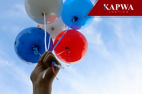 A person's hand holding a bunch of colorful balloons against a blue sky.
